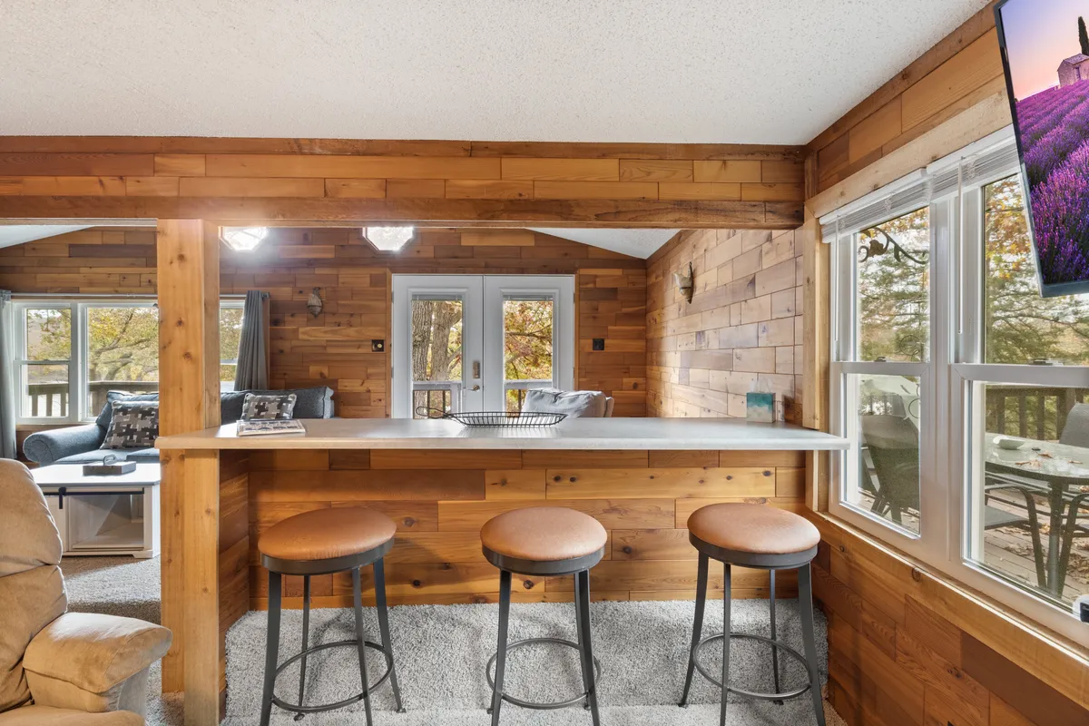 A social hub featuring a bar counter with stools, windows overlooking the exterior, wood paneling, and a television. The scene suggests both morning coffee and lively evenings, ideal for gatherings and family interactions.