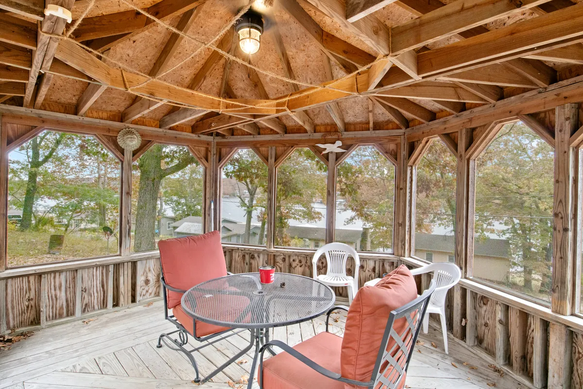 A round table with chairs under wooden ceiling beams, with large windows framing beautiful outdoor views. Soft morning light streams in, suggesting a serene spot for coffee or heartfelt conversation.