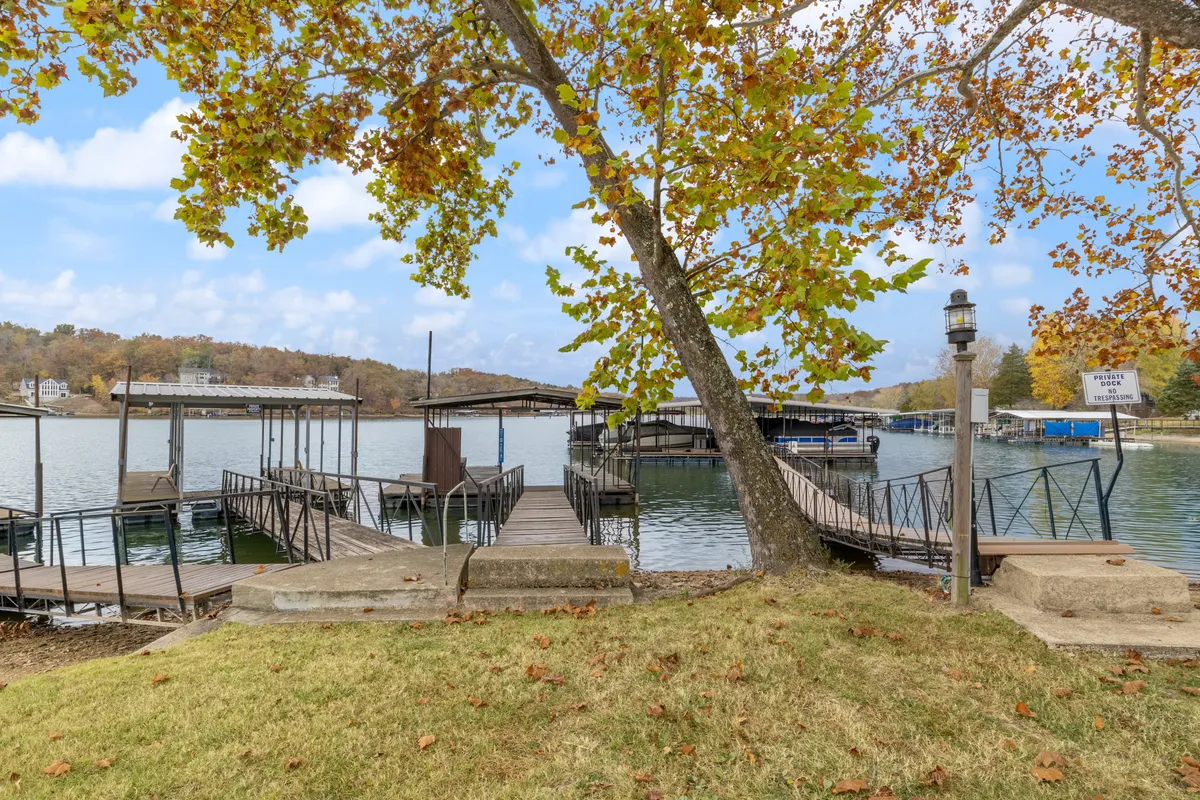 The hero image showcases a serene lakefront scene with a private dock extending over calm water, surrounded by vibrant autumn trees. Sunset reflections dance across the lake, and a lamp post softly illuminates the dock, inviting relaxation. Fishing poles rest nearby, hinting at leisurely mornings by the water.