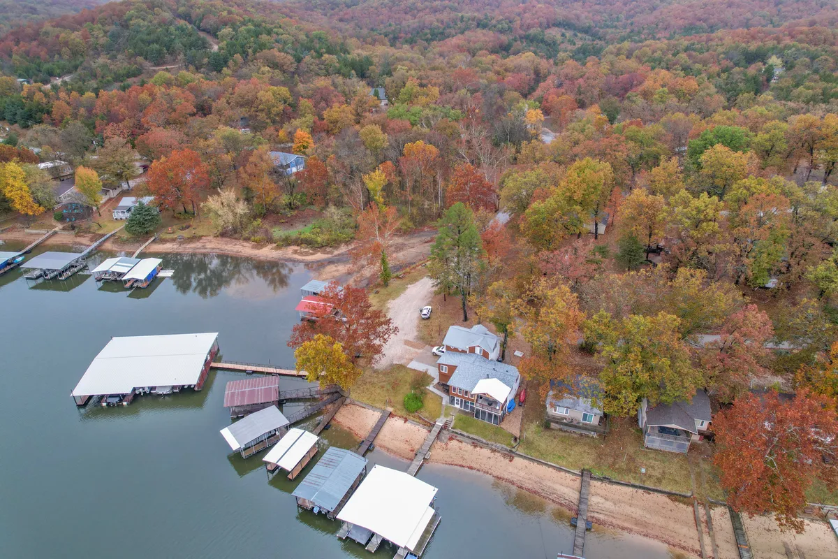 A tranquil exterior shot showing the lake, vibrant fall foliage, cozy cabins, and several docks extending into the water. The scene conveys a peaceful atmosphere ideal for relaxation or activity.