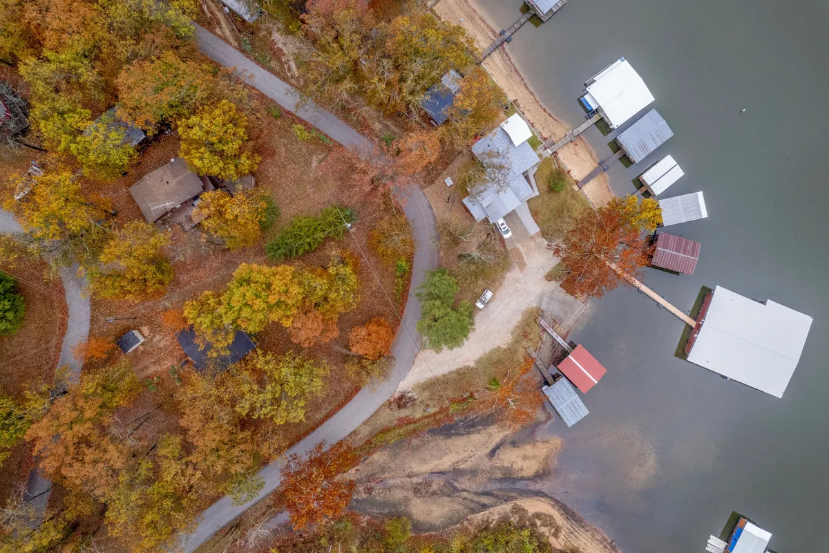 A panoramic lakeside view with multiple docks, lakeside homes, trees, and winding paths. The lake glistens in the light, inviting exploration and water activities.