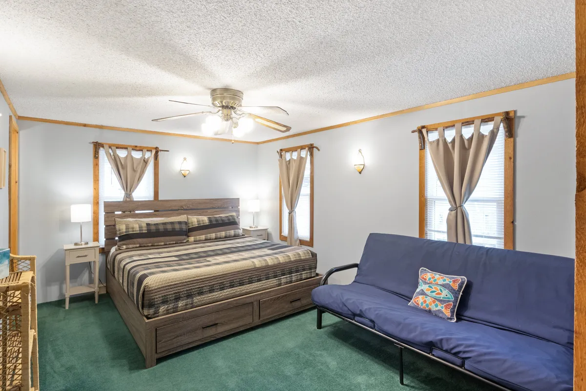 A welcoming interior space featuring a comfortable bed, a futon for extra sleeping arrangements, windows letting in natural light, and conveniently placed nightstands. The cozy atmosphere is ideal for families or friends needing flexible sleeping solutions.