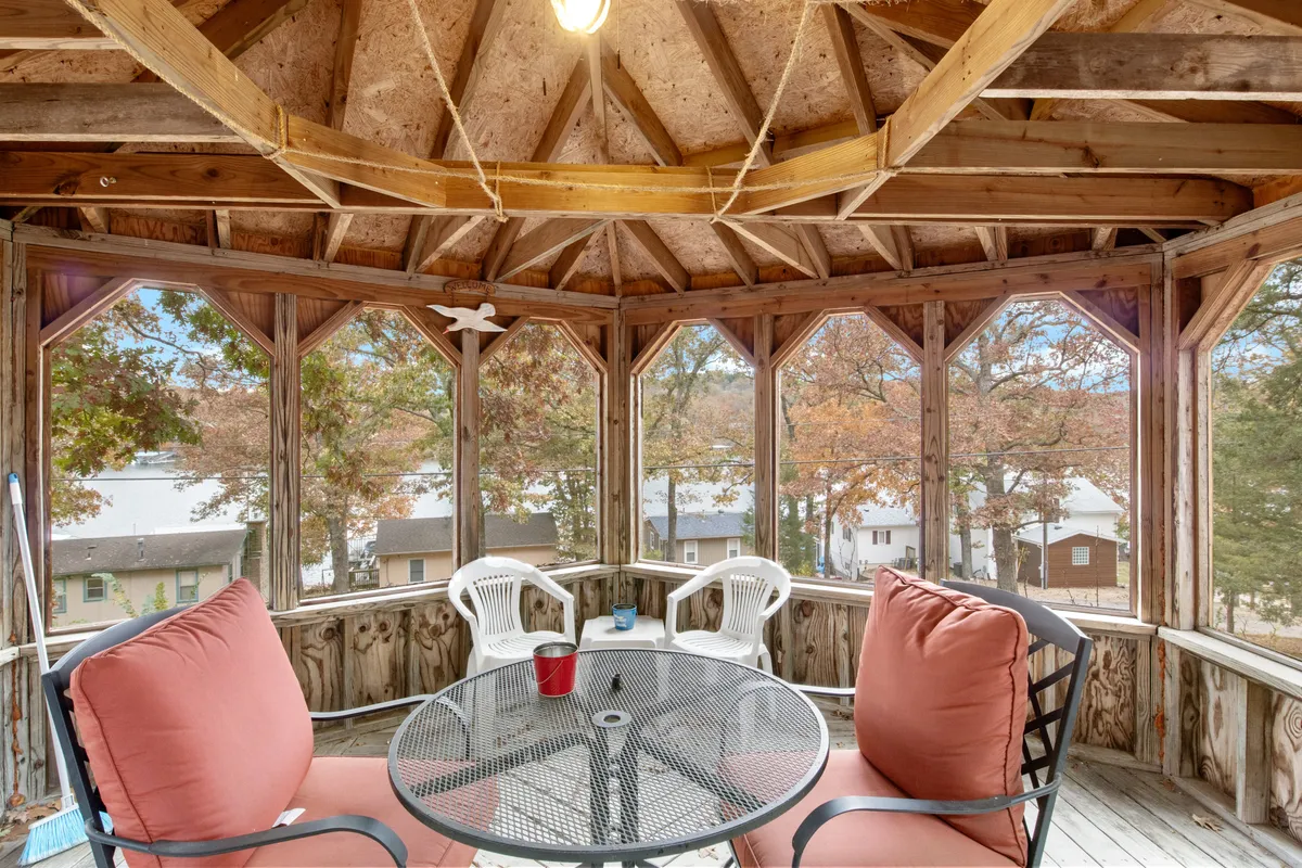 A sunlit indoor dining area features a round glass-top table with pink-cushioned chairs, offering views of the surrounding trees through large windows. The space is comfortable, airy, and designed for casual meals and intimate gatherings.