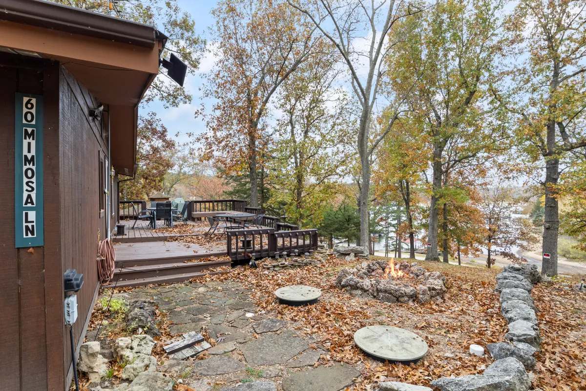 A cozy fire pit and deck surrounded by trees, complete with comfortable patio furniture and the vivid colors of autumn, ready for outdoor gatherings, grilling, or quiet moments by the fire.