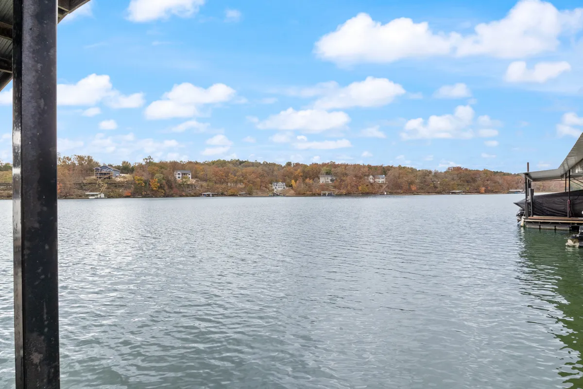 A tranquil lakeside scene featuring calm water, vibrant autumn foliage along the shoreline, and distant homes, with an inviting natural ambiance perfect for outdoor activities such as boating or nature walks.