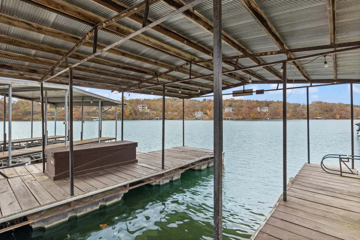A serene view of a dock area extending over quiet lake waters and surrounded by leafy trees, perfect for swimming, boating, or peaceful relaxation by the water. The atmosphere is tranquil, inviting moments of lakeside bliss.