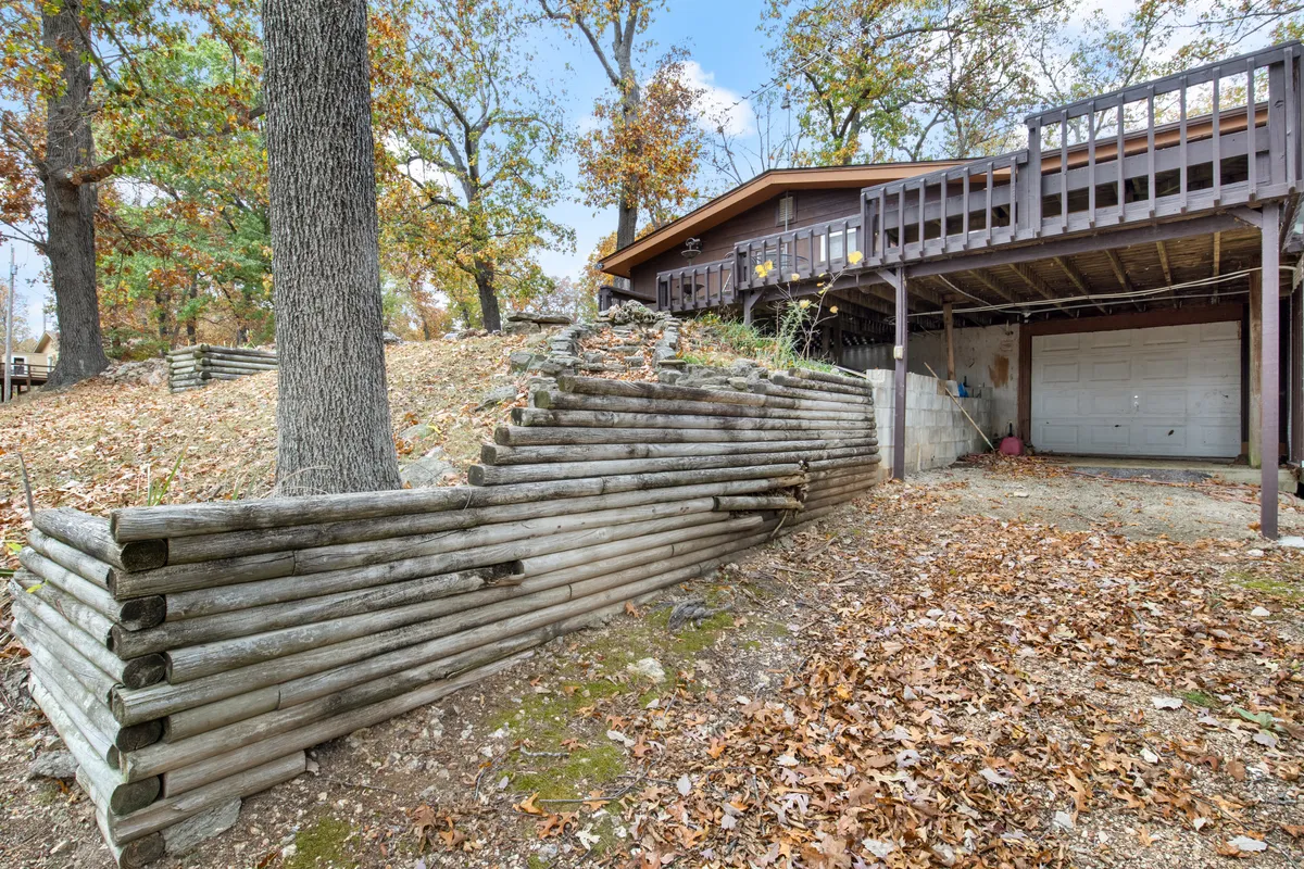 This image captures the inviting wooden log wall, attached deck, and garage door, all set against a backdrop of changing leaves and soft evening light. The space is ideal for outdoor gatherings or quiet evenings under the stars, emphasizing comfort and safety in a natural setting.