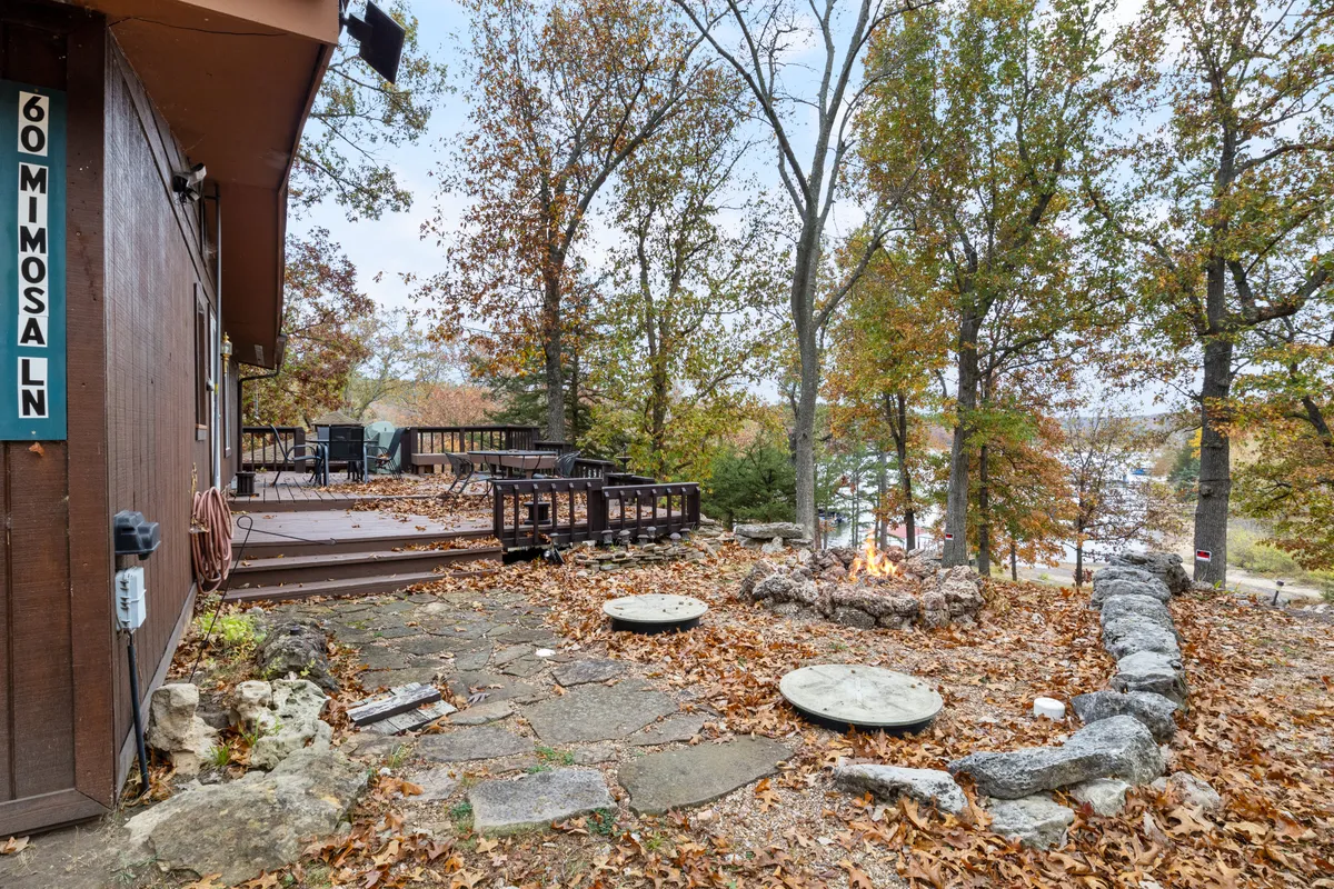 A cozy deck area with a stone fire pit, lounge seating, and a stone pathway leading towards the water. The setup is perfect for sunset gatherings, stargazing, or relaxing by the fire, all with a view of the lake in the background.