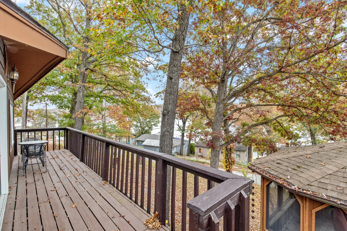 A spacious wooden deck nestled among tall trees with ample seating, ideal for social gatherings or relaxed family meals. The view extends to neighboring structures, emphasizing a communal atmosphere amidst natural beauty.
